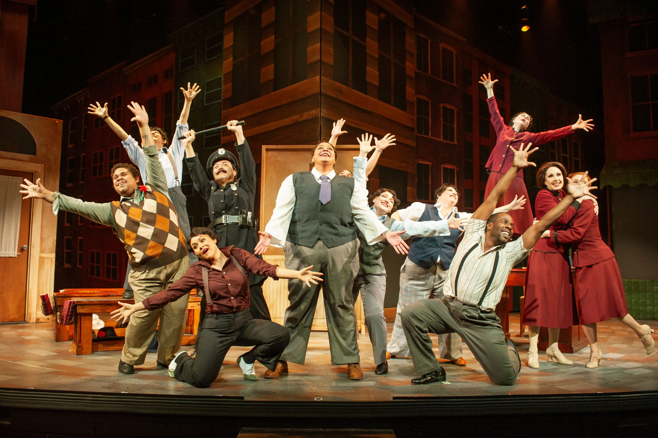 An ensemble of performers onstage at San Francisco Playhouse, with arms raised during a musical number.