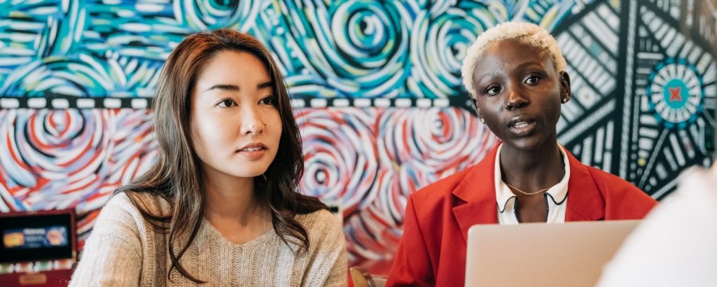 Focused diverse coworkers in trendy clothes discussing details of project while browsing laptop in modern workspace with creative interior in daytime